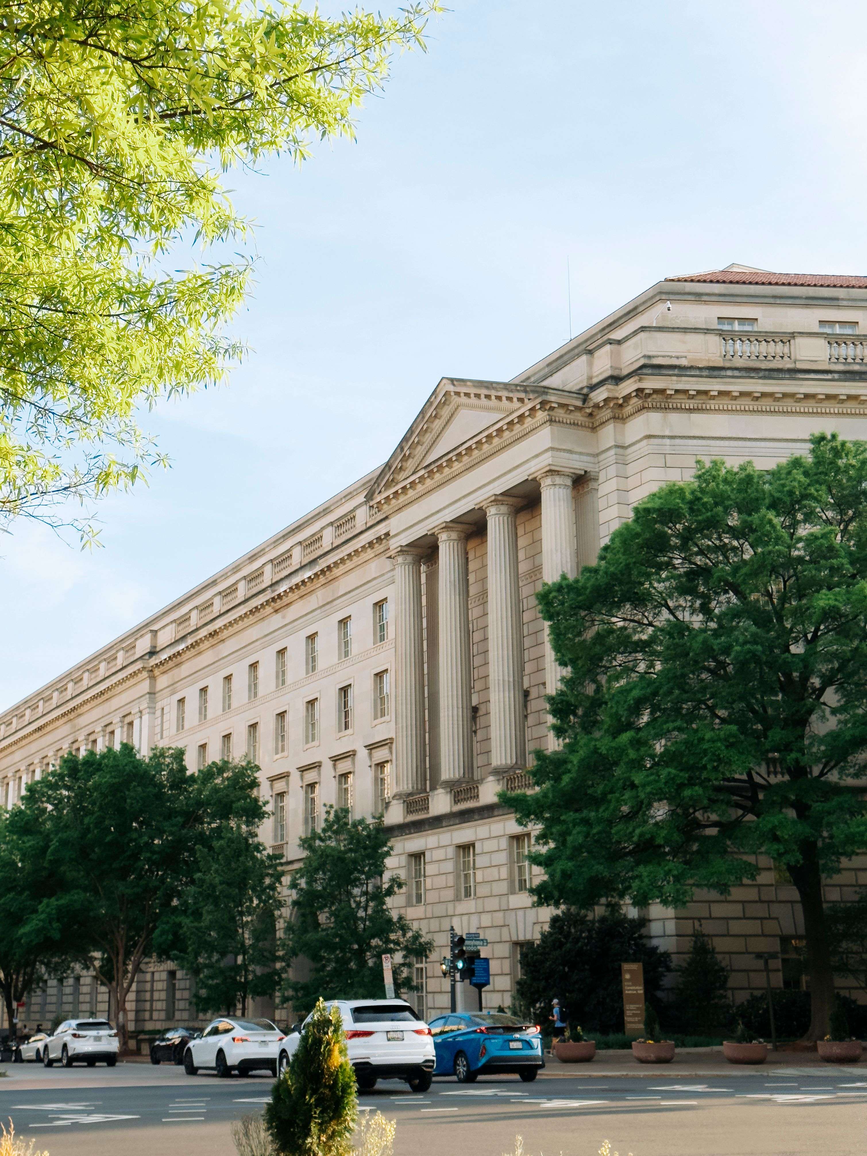 Neoclassical government building with a colonnaded stone facade behind mature trees — the kind of public-sector facility EntryBit secures